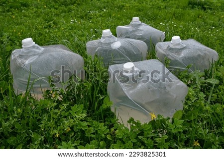 transparent plastic cube for water storage , on green grass.a plastic jug being filled with water. Royalty-Free Stock Photo #2293825301