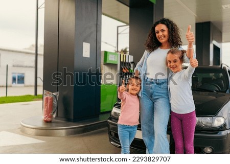 Mother and daughters pose for a picture in front of a car at a gas station before going on a family trip