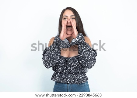 young brunette woman wearing a blouse over white studio background shouting excited to front.