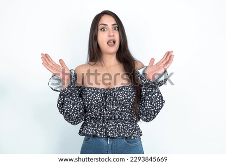 Surprised terrified young brunette woman wearing a blouse over white studio background Gestures with uncertainty, stares at camera, puzzled as doesn't know answer on tricky question, People, body lang
