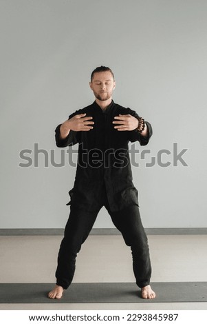 A man in black kimano practicing qigong energy exercises indoors. Royalty-Free Stock Photo #2293845987