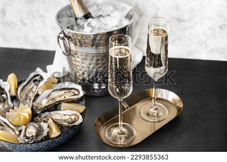 Champagne glasses with sparkling wine and bottle in bucket near oysters Royalty-Free Stock Photo #2293855363