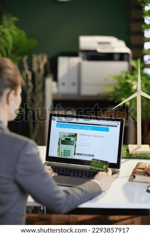 Seen from behind modern business woman with laptop and credit card browsing online shop in modern office.