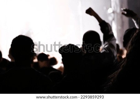 Cheering crowd and stage lights with space for your text. Defocus silhouette of people raise hand up in music concert with black and yellow color spotlight on stage background. Out of focus. Royalty-Free Stock Photo #2293859293