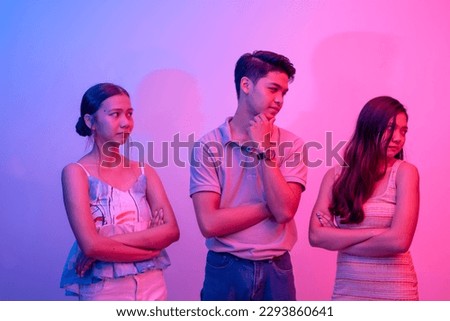 Two women are not pleased with a two timing playboy trying to hit on both of them. Party scene lit with pink and blue neon colors. Royalty-Free Stock Photo #2293860641