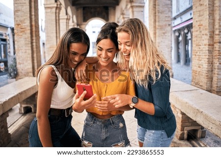 Three happy women using mobile phone outdoors. Group of smiling female friends watching social media at smartphone. High quality photo Royalty-Free Stock Photo #2293865553