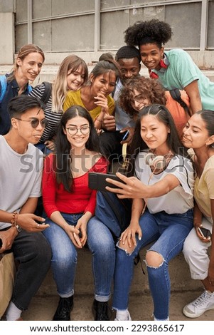 Vertical photo of a group of multi-ethnic students taking selfies with mobile phone. Teenagers using a smart phone and having fun together.