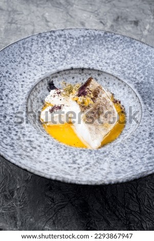 Modern style traditional sauteed skrei cod fish filet with skin with creme fraiche quenelles and algae in passion fruit sauce in ceramic design plate as close-up 