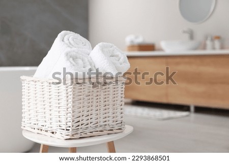 Wicker basket with fresh white towels on stool in bathroom. Space for text Royalty-Free Stock Photo #2293868501