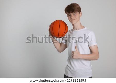 Teenage boy with basketball ball showing thumbs up on light grey background. Space for text