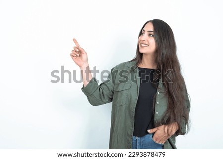 Smiling young brunette woman wearing casual clothes over white studio background indicating finger empty space showing best low prices