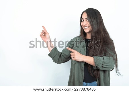 young brunette woman wearing casual clothes over white studio background indicating finger empty space showing best low prices, looking at the camera