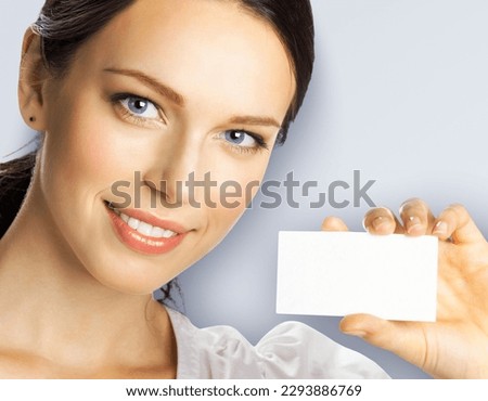 Portrait of smiling businesswoman showing mockup empty businesscard or plastic credit card, with copy space for sign, light grey gray background. Brunette business woman at studio image.