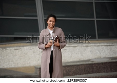 Happy african american woman in business clothes goes to a meeting in the office with a notepad and coffee.Portrait of a successful business woman near the business center. Management concept.