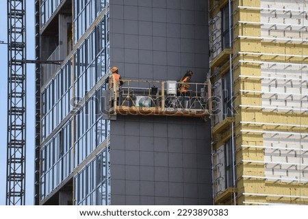 Workers sheathe the outer walls of a brick house with insulation. Insulation of the facade of the building. The concept of exterior decoration, moisture protection, sound insulation, energy saving. Royalty-Free Stock Photo #2293890383