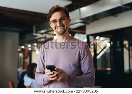 Portrait of a happy business man holding a cellphone in an office. Professional business man looking at the camera while standing in a workplace.