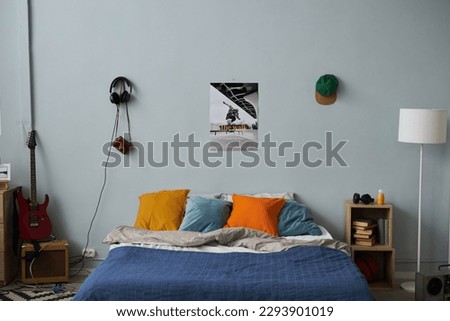 Part of spacious bedroom of teenager with comfortable double bed standing by grey wall with poster, cap and headphones Royalty-Free Stock Photo #2293901019