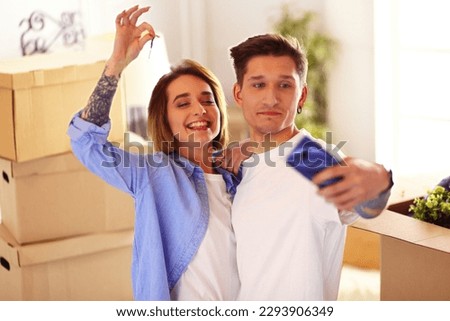 Young happy man and woman make selfie on smartphone, holding keys of new home after buying house apartment.