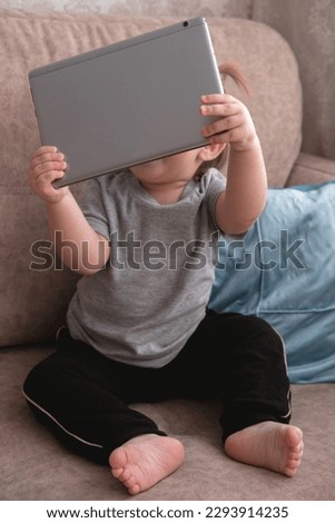Cute little girl sitting on sofa and using tablet.