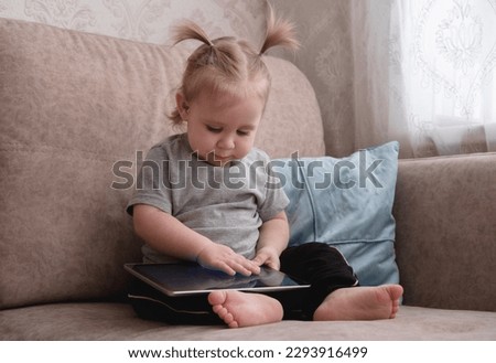 Cute little girl sitting on sofa and using tablet.