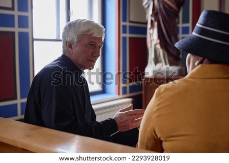 Senior priest discussing christian moments with woman while they sitting on bench in church