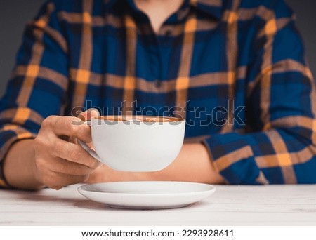 A man in a shirt holding a cup of coffee while sitting at the table. Close-up photo. Beverage and relaxation concept