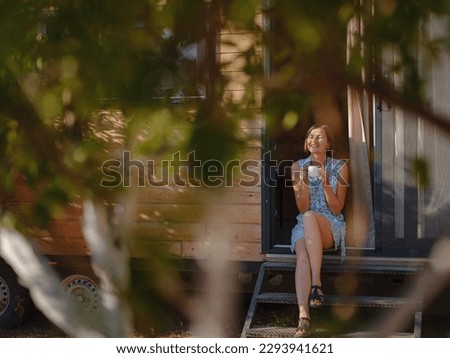 Woman is drinking coffee , morning routine near her Tiny house. First property. Small apartment in summer garden. Minimalism. Moving in. Living alone. Charming trailer house Royalty-Free Stock Photo #2293941621