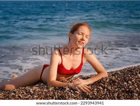Beautiful ginger woman in red bikini on tropical beach. Portrait of happy young lady smiling at sea. Happy girl with red hair and freckles enjoying the sun. concept of safe interaction with sun