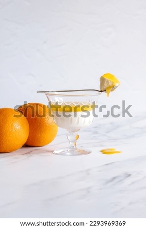 Vanilla bean panna cotta with orange jelly in a glass on a light and bright backdrop. 