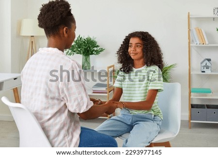 African american woman psychologist holding hands teen girl sitting in front of her at school. Girl in casual clothes looks at woman with trust and hope. Teens education, psychological help concept. Royalty-Free Stock Photo #2293977145