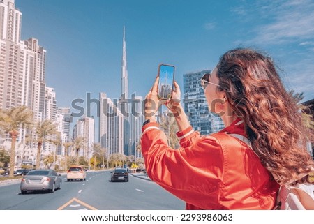 Tourist happy girl taking photos for her travel blog, in Dubai downtown district against background of the Burj Khalifa highest skyscraper Royalty-Free Stock Photo #2293986063