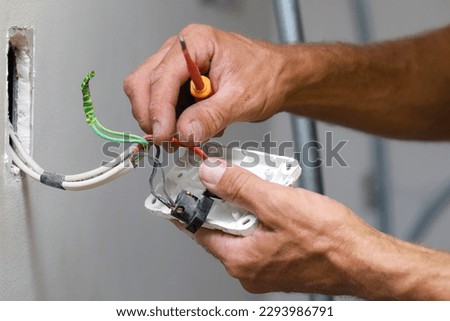 A close up of an electrician working on a light switch at a clients home.  Royalty-Free Stock Photo #2293986791