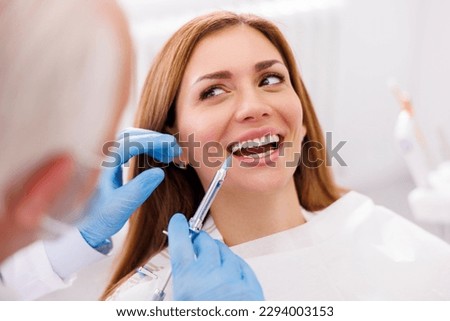 Detail of dentist applying local anesthetic to patient for numbing the pain before procedure; doctor applying lip fillers to female patient