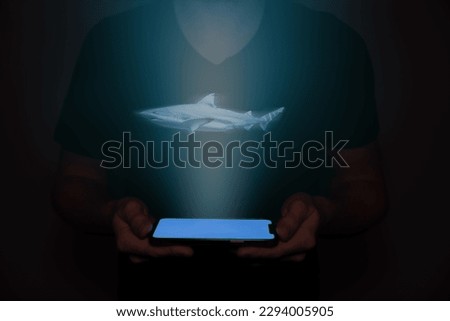 A man in the future holds a on which a shark is projected. New technology.