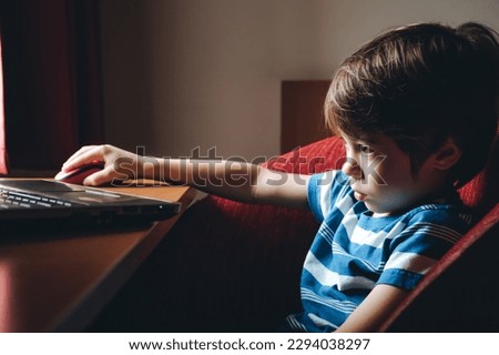 6 year boy looking at the laptop screen. Uses mouse. Watching cartoons or video. Home online education concept. The concentrating kid. Reads a task. 4K. Tired eyes. Parental content control. Too long.