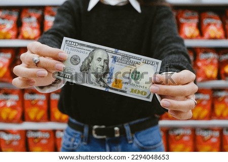 Woman Holding A 100 Dollar Bill In The Supermarket. Concept Of Inflation And Rise Of The Dollar In Argentina Royalty-Free Stock Photo #2294048653