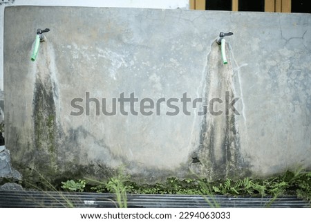 photo of a water faucet with a gray, mossy wall