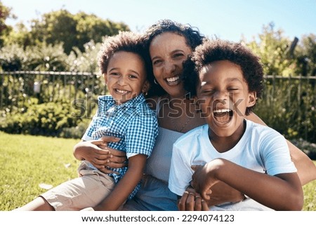 Excited little boy with afro sitting outside on the grass with his mother and brother. Energetic african american family spending time outdoors at the park or their backyard. Mom embracing two sons Royalty-Free Stock Photo #2294074123