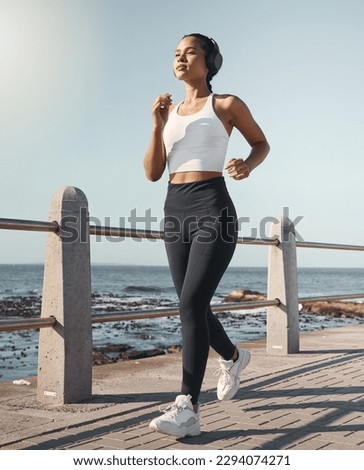 Young fit sportswoman wearing wireless headphones and listening to music while out for a run along the promenade. Exercise is good for you health and wellbeing