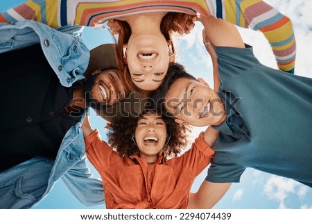 Group of diverse friends standing in a huddle against a blue sky. Multi-racial friends standing together arms around each other and smiling while looking down at the camera Royalty-Free Stock Photo #2294074439