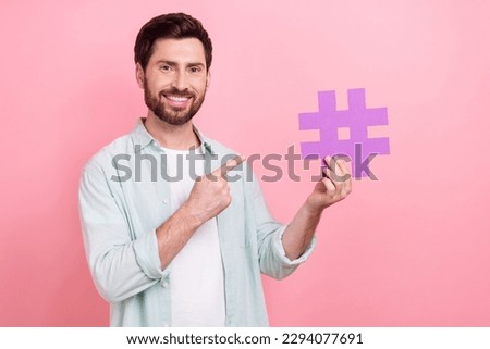 Photo portrait of handsome young guy hold number hashtag symbol blogger dressed stylish blue clothes isolated on pink color background