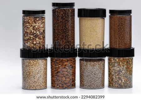 Loose products in the kitchen.  Stocks of grains, nuts and coffee stored in the kitchen in plastic airtight containers with black caps.  Side view on a light background Royalty-Free Stock Photo #2294082399