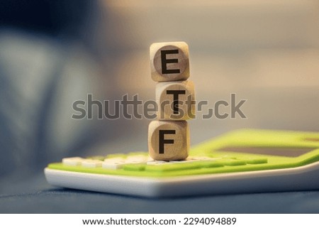 ETF acronym for Exchange Traded Fund written on wooden dice that are stacked. A calculator and a blue sofa in the composition. Close-up photo.
