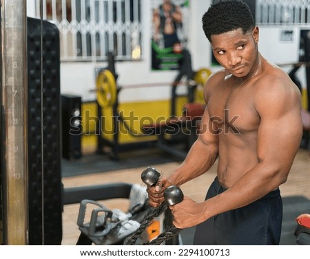 A muscular young adult athlete, determinedly using weight training and cross-training in a health club gym to sculpt their bodybuilder physique.