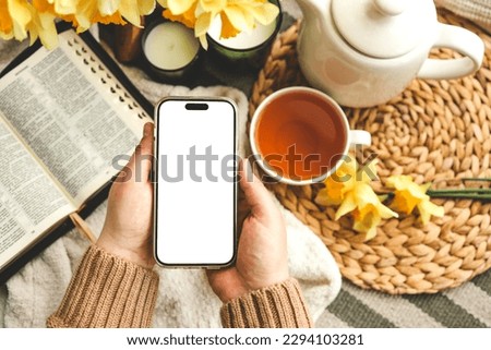 Phone with an isolated screen in hands against the background of the Bible, aesthetic spring composition.