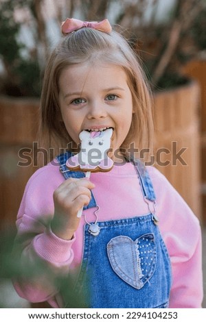 A beautiful pretty girl in pink clothes with a bow on her head eats gingerbread in the form of a unicorn. Childhood. Sweets.