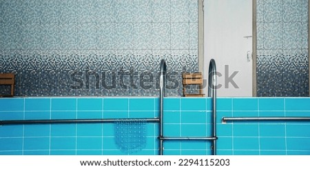 Pool interior with blue tiled wall and metal ladder with handrail. Swimming practice and training concept.