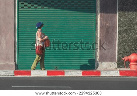 Asian female Tourist in protective mask is Walking on pedestrian walkway with sunlight and shadow on building wall background, Street photo style