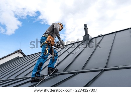 Work at heights. A roofer with tool belt and save harness climbing to the top of the roof. Royalty-Free Stock Photo #2294127807