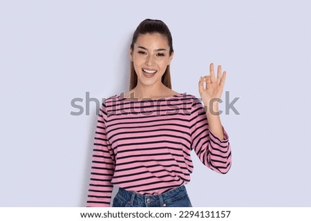 Positive smiling beautiful latin young woman in casual outfit showing okay gesture and smiling at camera on grey studio background, copy space. Emotions. gestures concept